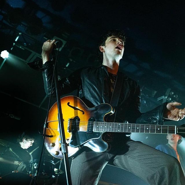 Elijah Hewson in a black leather jacket and grey pants performing on the stage.